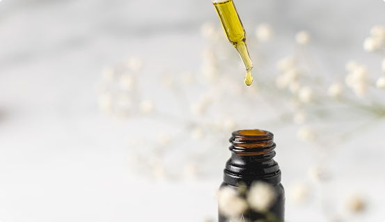 Amber glass bottle with CBD oil dropper and oil drop on light floral background