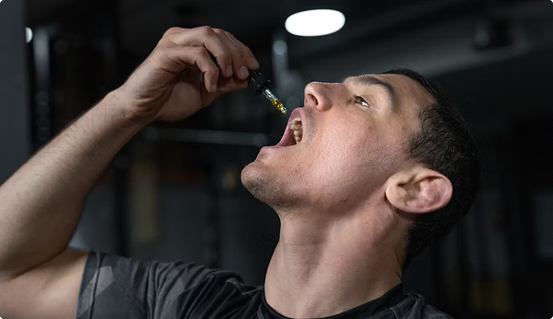Man taking CBD oil with dropper for wellness in a gym setting